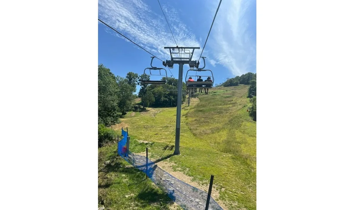 An inviting exterior shot featuring a ski lift ascending a lush green hillside beneath a vibrant blue sky. The landscape suggests expansive natural surroundings and easy access to outdoor adventures, including hiking and exploring with pets.