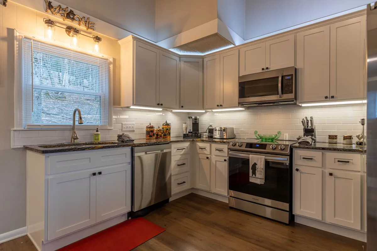 This image showcases the kitchen's central island, stainless steel appliances, and gleaming granite countertops. The workspace is warmly lit, inviting, and clearly equipped for both cooking and gathering, with comfortable space around the island for guests to mingle or help with meal prep.