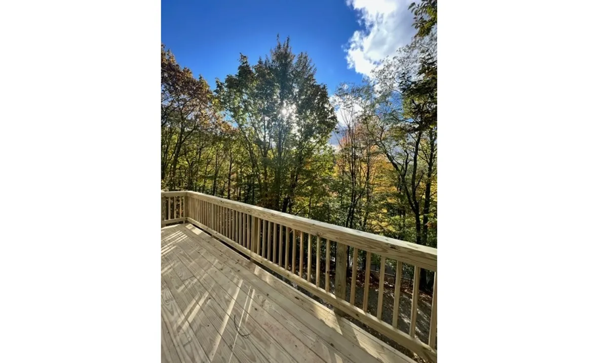 A peaceful view from the wooden railing of the lodge deck, looking out at the surrounding trees and open sky. The tranquil atmosphere is ideal for noticing wildlife, listening to birds, or enjoying the sunset and stargazing.