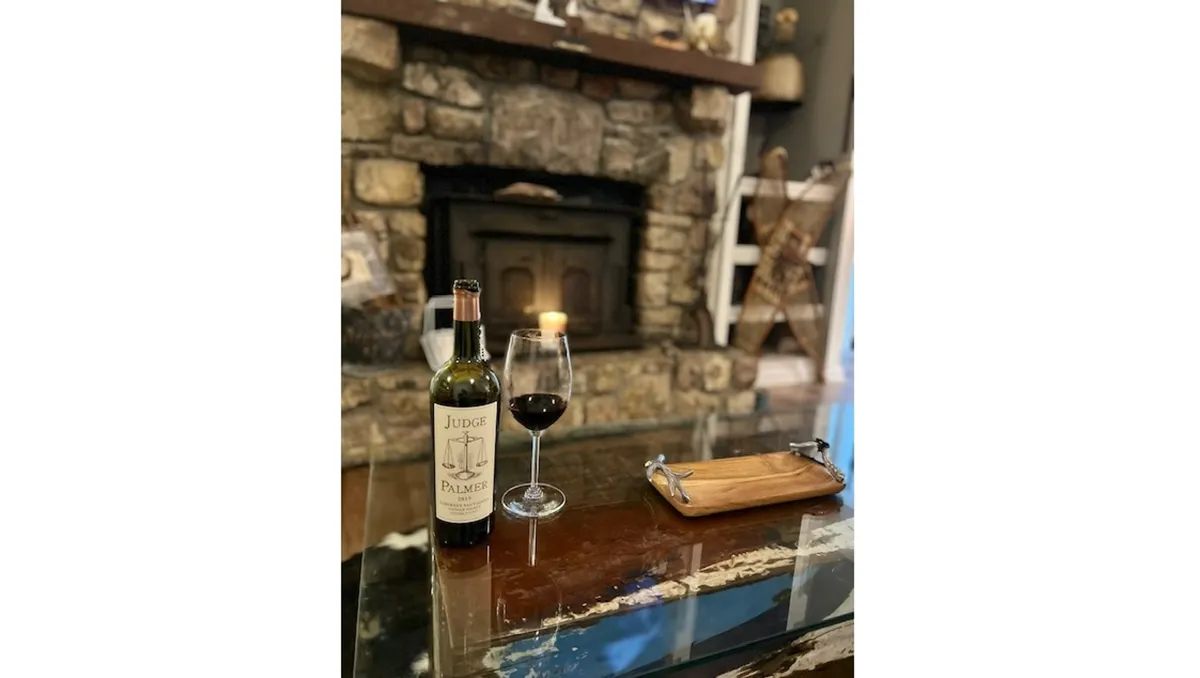 A close-up of a wooden tray set with a wine bottle and glasses in front of a crackling fireplace, inviting guests to unwind and celebrate in a cozy, fire-lit atmosphere.