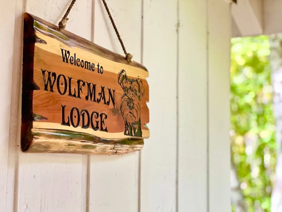 A rustic wooden sign reading 'Wolfman Lodge', complete with a carved wolf illustration, welcoming guests into the property. The sign embodies a sense of arrival and adventure, inviting guests and their pets to begin their stay.