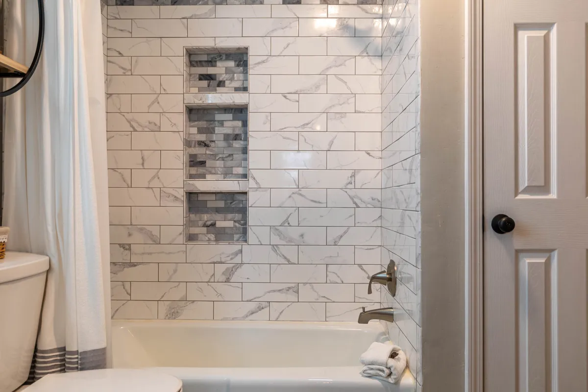 A spa-inspired bathroom with a marble tile pattern, a bathtub perfect for soaking, a shower curtain, and a decorative niche with stones. The space is bright and calming, designed for relaxation and rejuvenation after a long day.