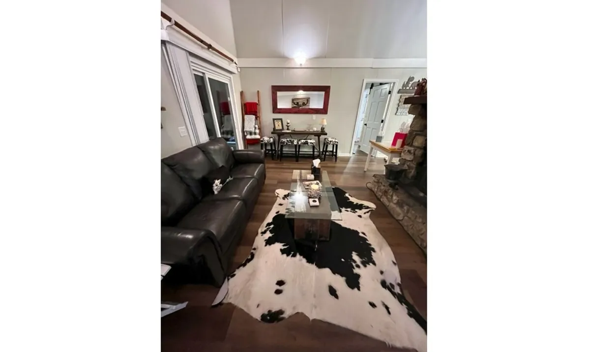 A plush leather sofa and cowhide rug create a cozy living space, with a wood-burning fireplace as the focal point. The dining area is visible in the background, emphasizing the open flow between living, dining, and kitchen spaces.